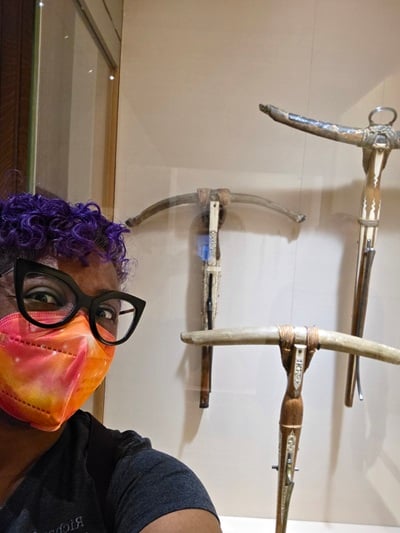 Patricia wearing a KN95 mask in front of a museum display of crossbows.