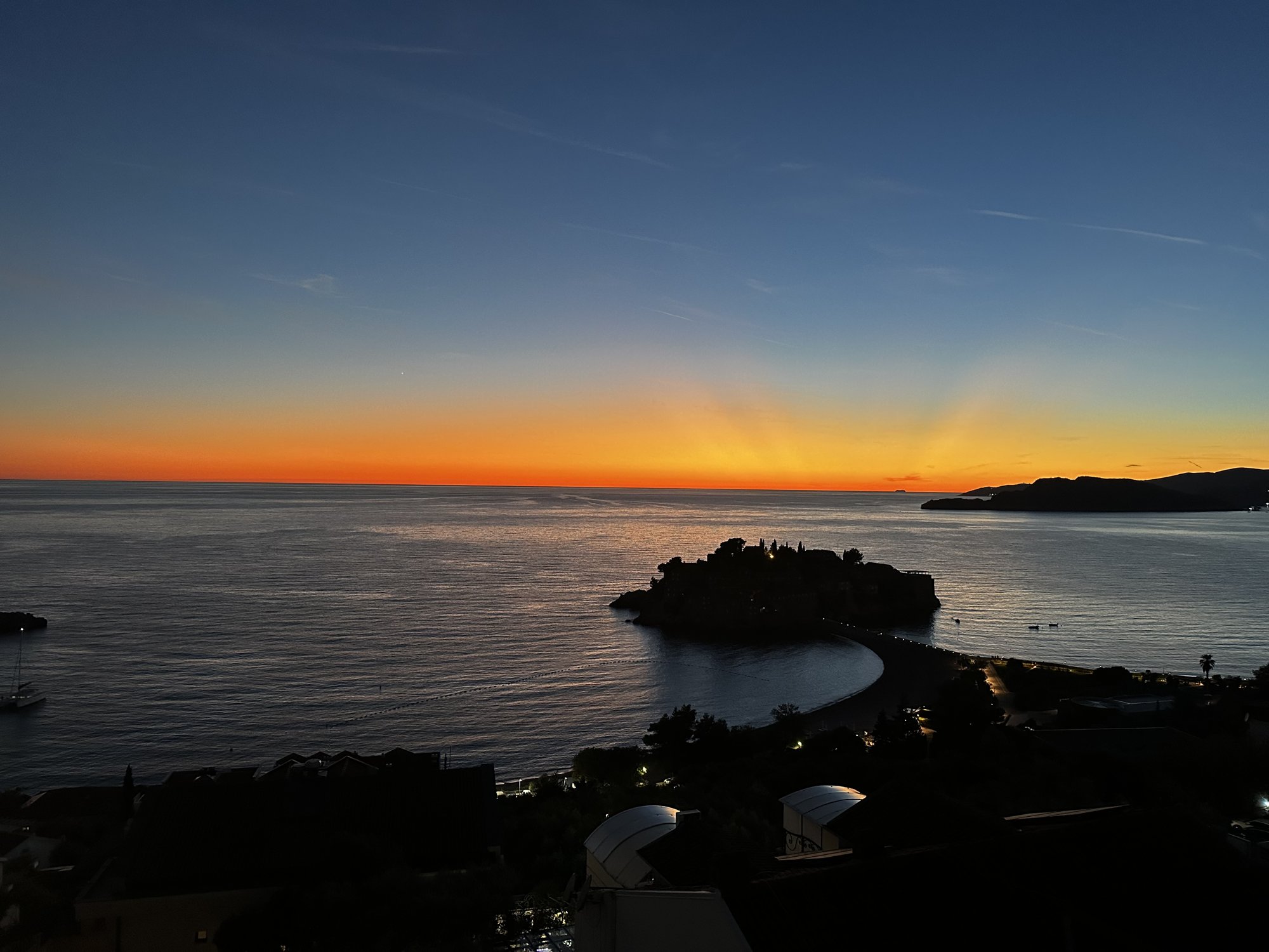 Sveti Stefan island silhouetted against an orange sunset over the Adriatic