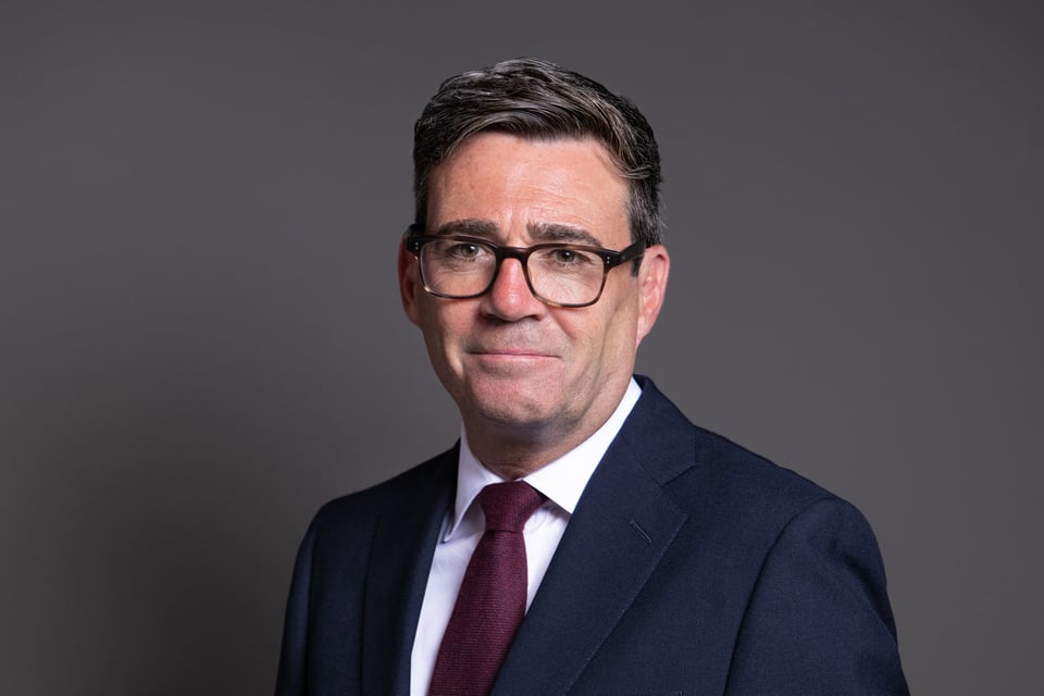 A white man with short dark brown hair, rimmed glasses, and a suit with a burgundy tie