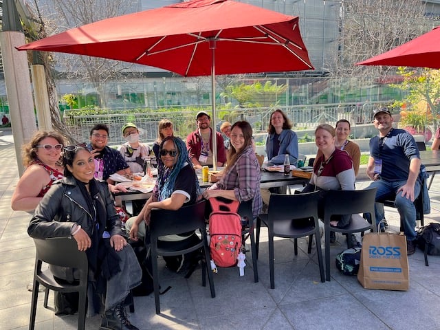 A large group of people sitting around a table in the sunshine