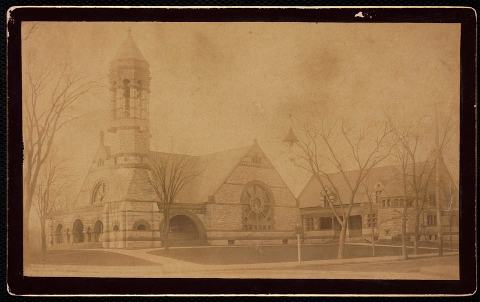 A sepia-toned photograph of a Romanesque Revival church with a tower