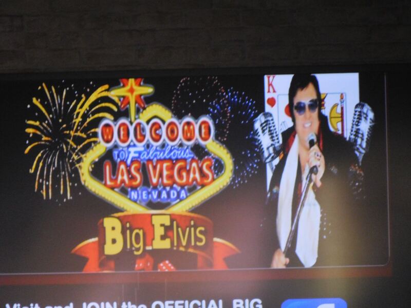 An electronic display with images of a large man dressed as Elvis Presley, the iconic "Welcome to Fabulous Las Vegas Nevada" sign, and a banner reading, "Big Elivs."