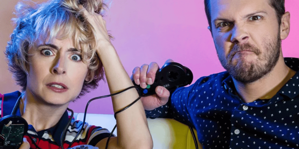 Greg and Heather pose with game controllers and look angry.
