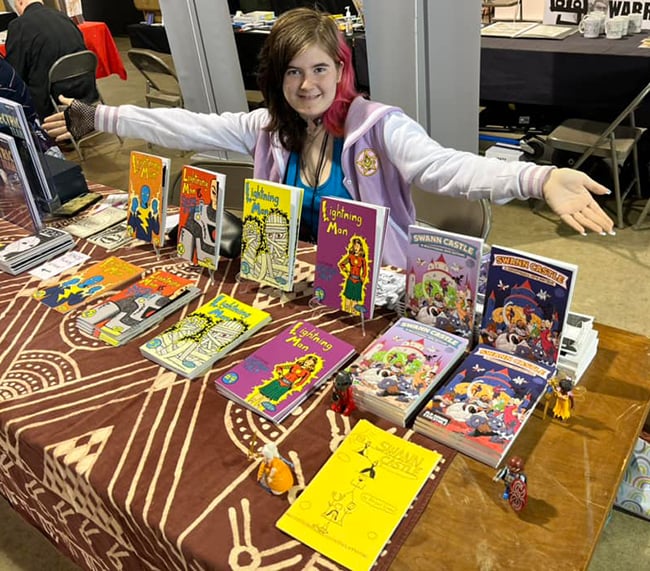 A teenager sitting at a table, behind a display of colorful comics.