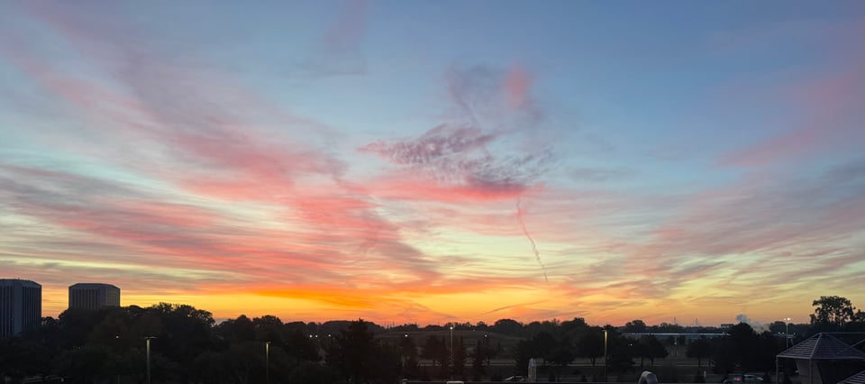 photo of varicolored sunrise from hotel window, with a few tall buildings on the horizon