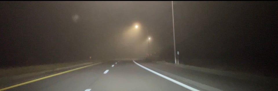 A nighttime photo of fogged-up lamps shining on a two-lane highway
