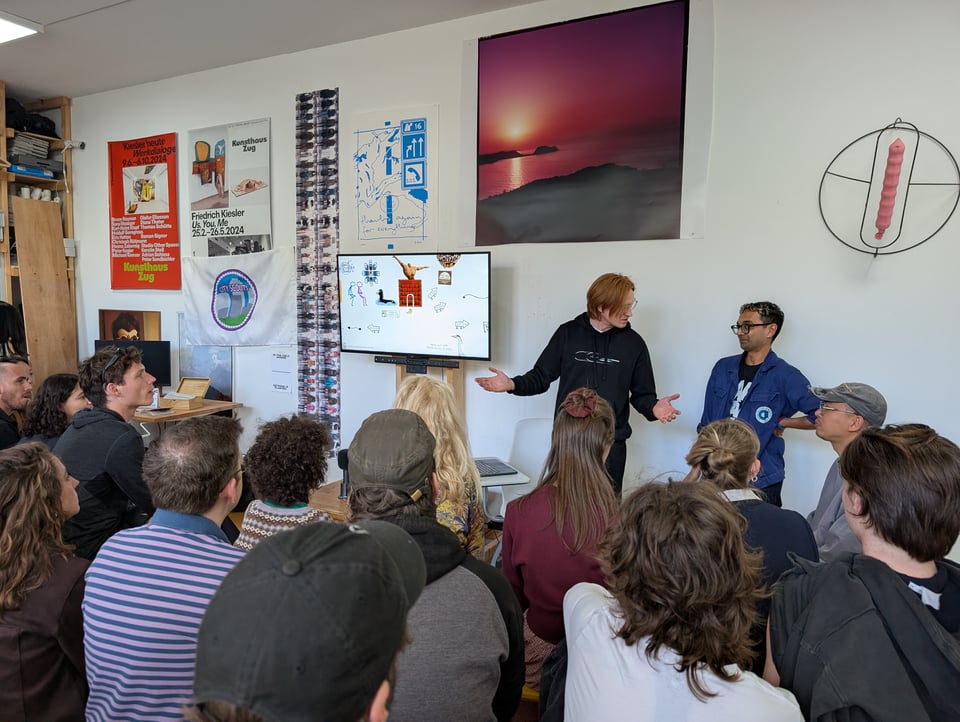 Three hosts gesture and talk among each other in front of an expectant crowd.