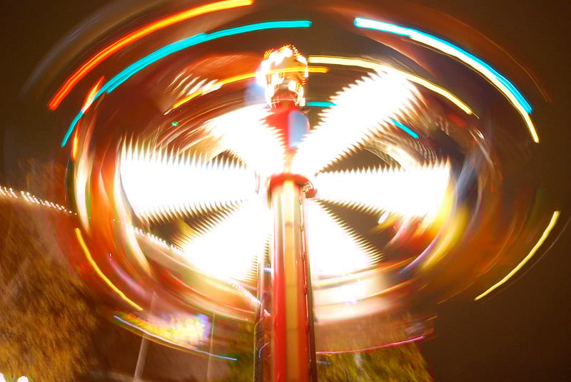 A carnival ride spins at high speed, causing the lights and riders to blur.