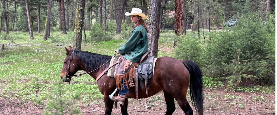 Photo shows JMC student Olivia Schaefer atop a horse, wearing large white cowboy hat and a green jacket.