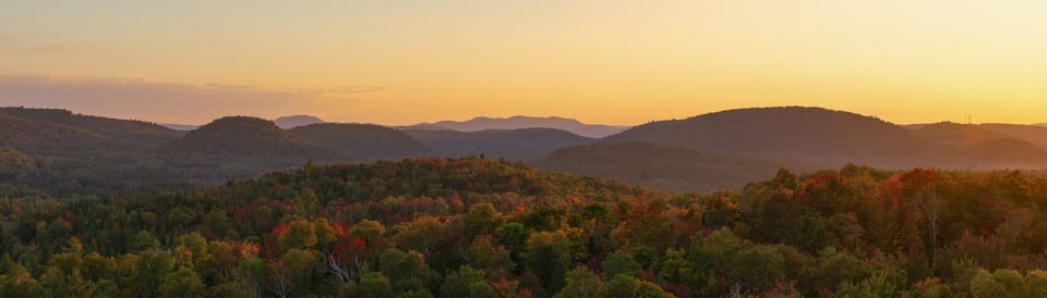 a golden sunrise over low mountains that have some fall leaves
