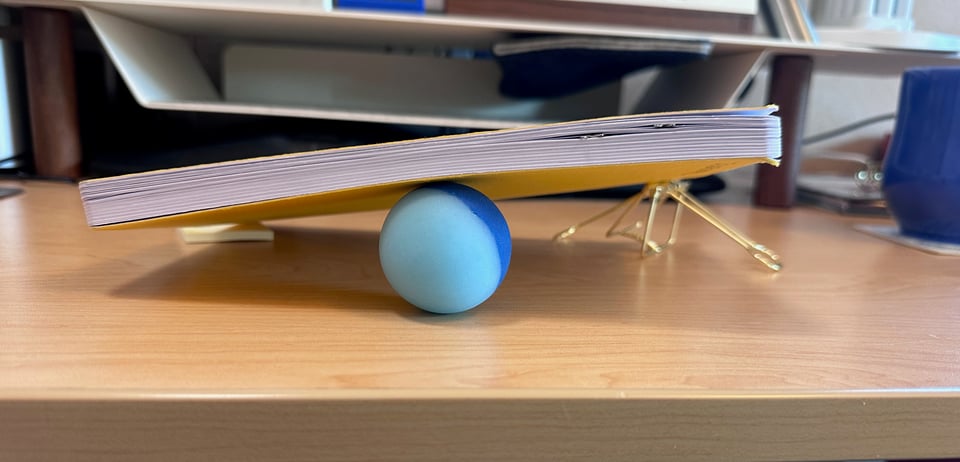 A notebook balanced on three stray items from the writer's desktop. It looks very stable.