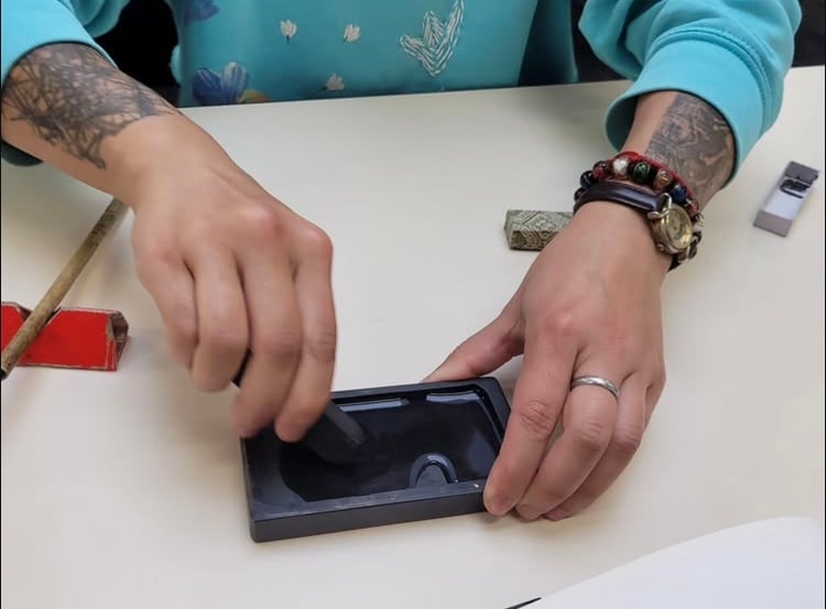 A person grinds a stick of ink onto an inkstone