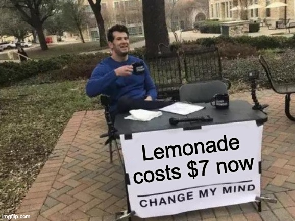 The Change My Mind meme: white guy sits behind table with a coffee cup in his hand, with a sign taped to the table that reads: "Lemonade costs $7 now - CHANGE MY MIND"