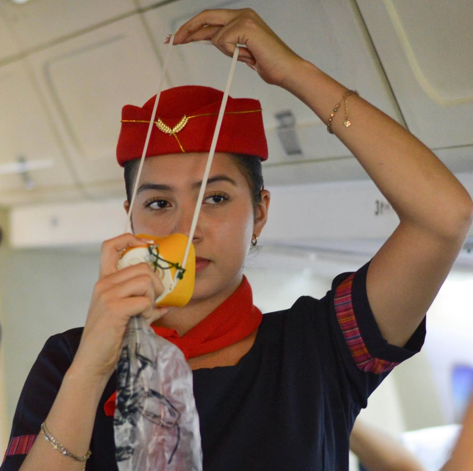Stewardess is about to cover her nose and mouth with the yellow plastic mask with attached air bag.