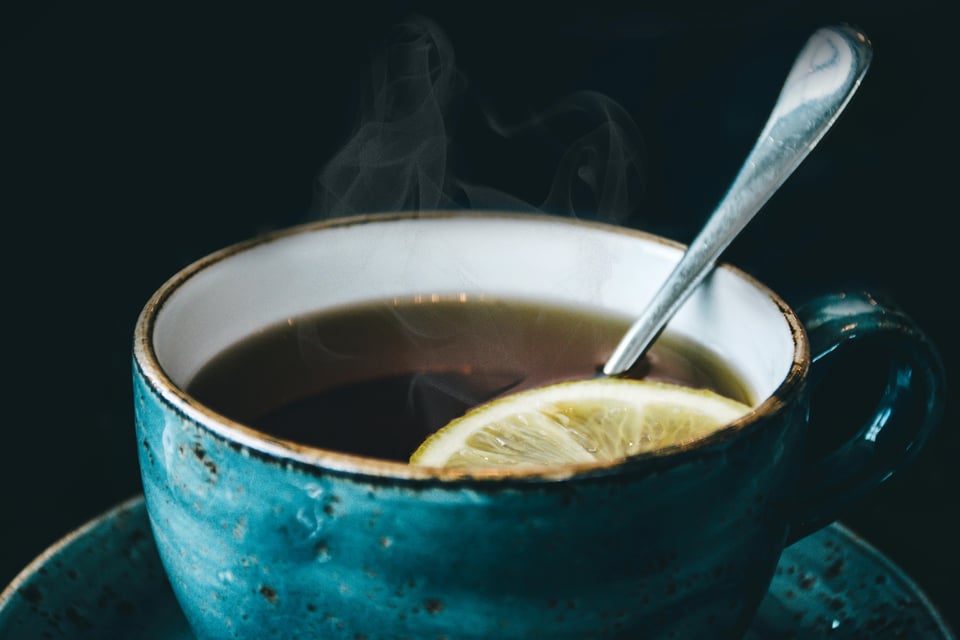 A close-up of a blue ceramic cup with dark brown tea and a slice of lemon.