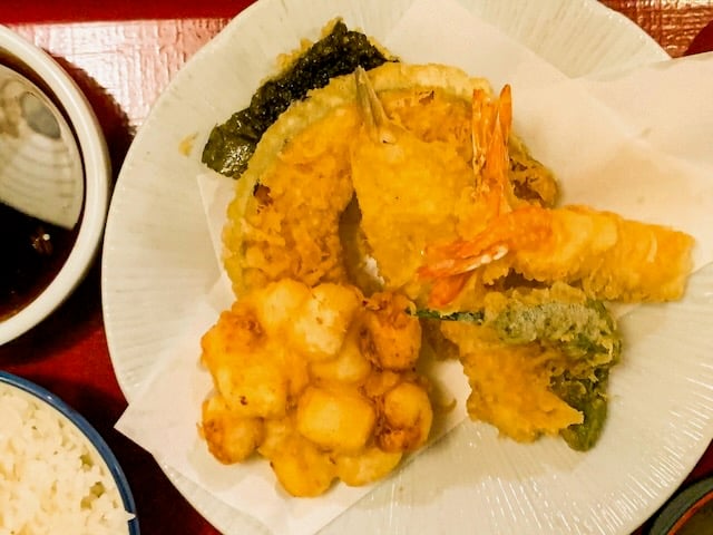 A pile of tempura, including shrimp and squash, sits on a white plate on a red tray
