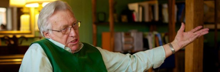 Wes Jackson, his left arm outstretched, in front of bookshelves in his study