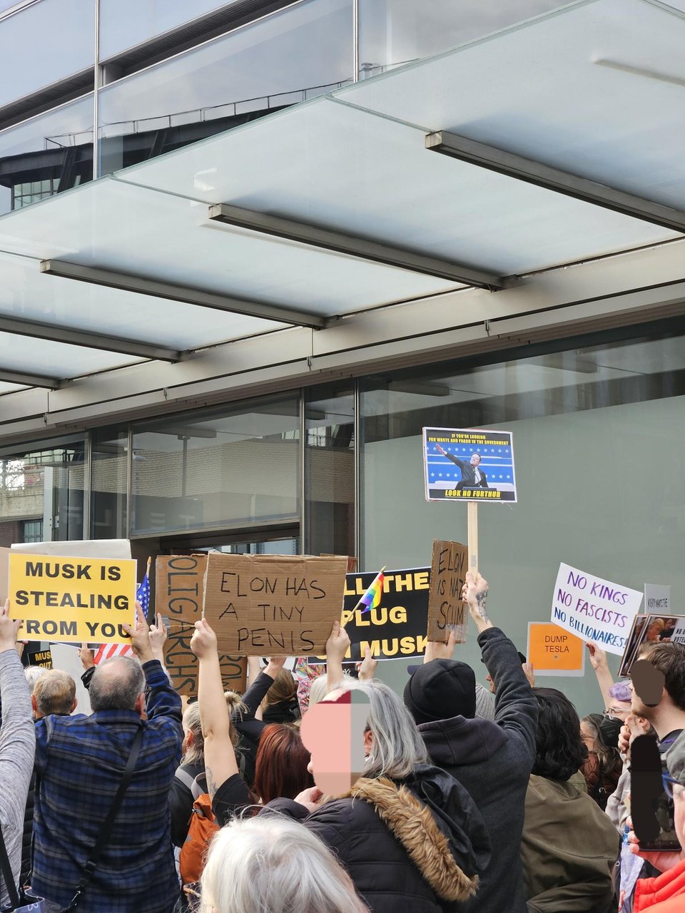 Photo from a Tesla takedown protest in NYC. People are carrying signs saying Musk Is Stealing from you. No Kings, No Fascists, No Billionaire, and Dump Tesla.