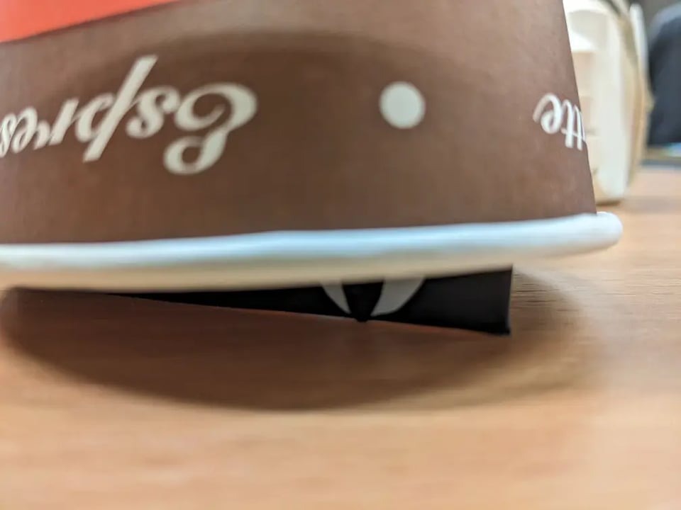 A close up of an upside down paper cup, showing a black shim with an eye peeking from underneath.