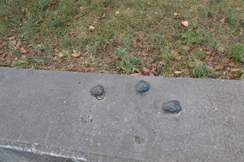 Three little bronze frogs on the top of a wall.