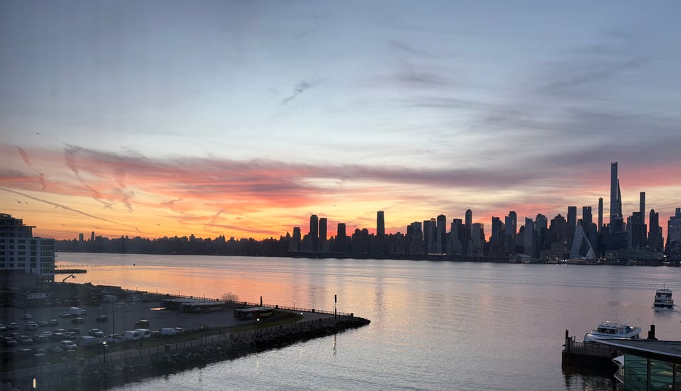 view of sunrise over Manhattan skyline, with clouds illuminated in pink and gold