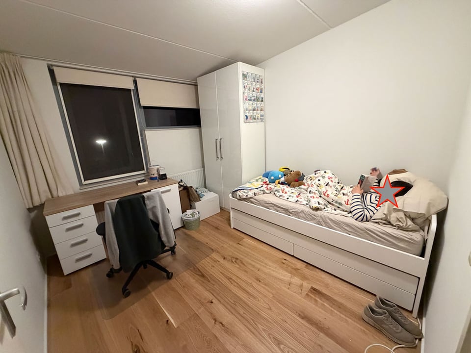A children's room is coming together with a desk, a closet and a bed. A young boy reads in bed.