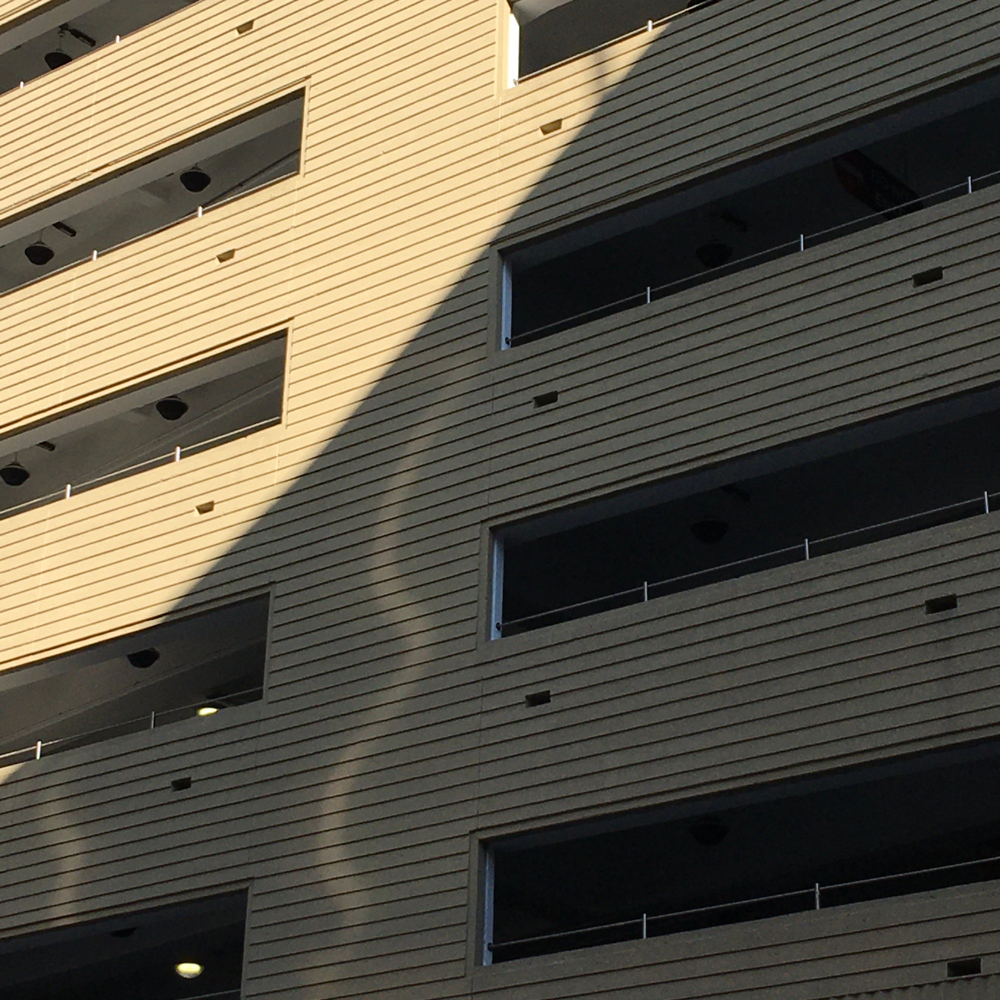 Photo depicts a close-up frame of a public parking structure, divided in half by light and shadow. In the shadowed area, there is a wiggle of light that streams down the garage.