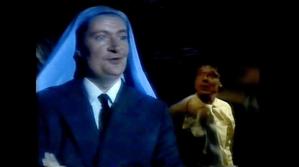 A younger Jim Broadbent stands wearing a suit and tie, and Mary's characteristic blue wimple, in a recorded stage production of The Messiah.