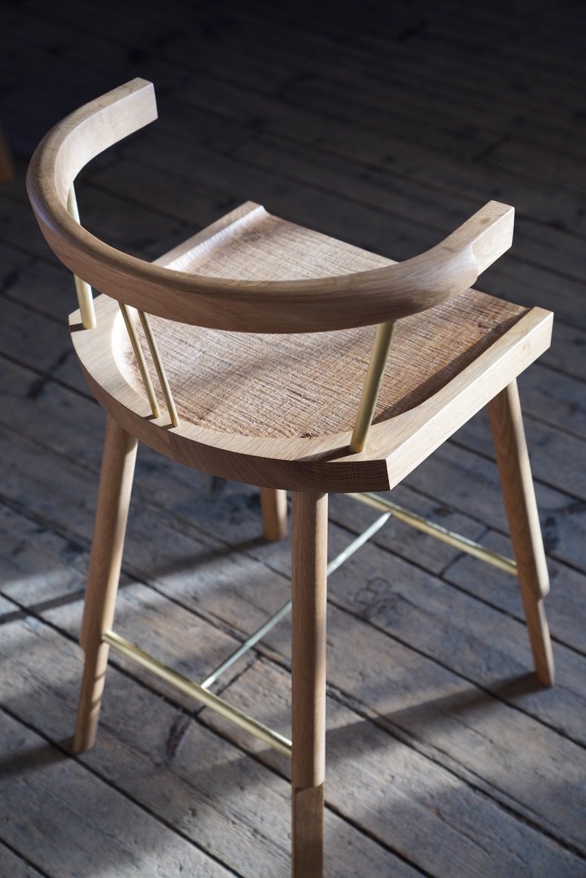 A wooden chair with brass rungs and spindles sits on a wooden deck in late afternoon sunlight.