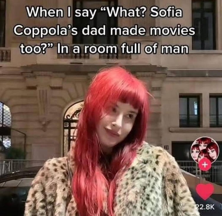 A photo of a pale woman with red lipstick and long red hair with a slight smirk and her head tilted (I would describe her vibe as "cheeky"). Overlaid text reads: When I say "What? Sofia Coppola's dad made movies too?" In a room full of man