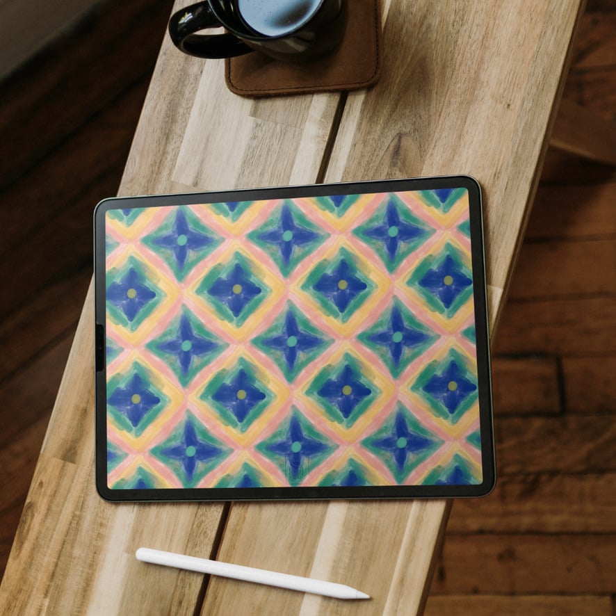 Image of a blue, green, pink, and yellow iPad wallpaper. iPad and pencil is sitting on a wooden bench with a cup of coffee.
