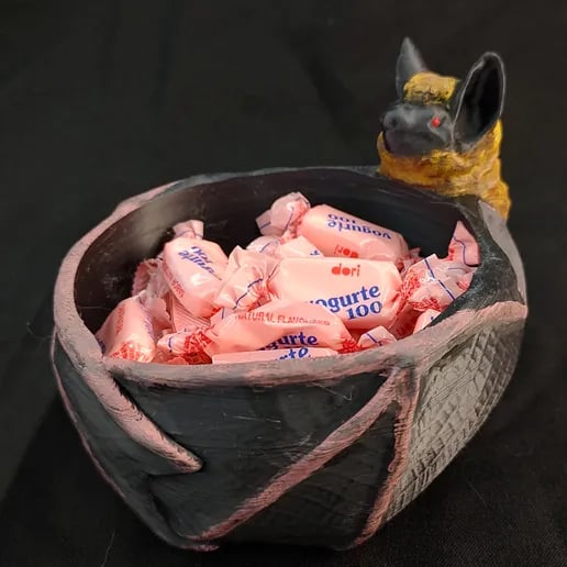 A bat wraps its wings around a bowl of candy