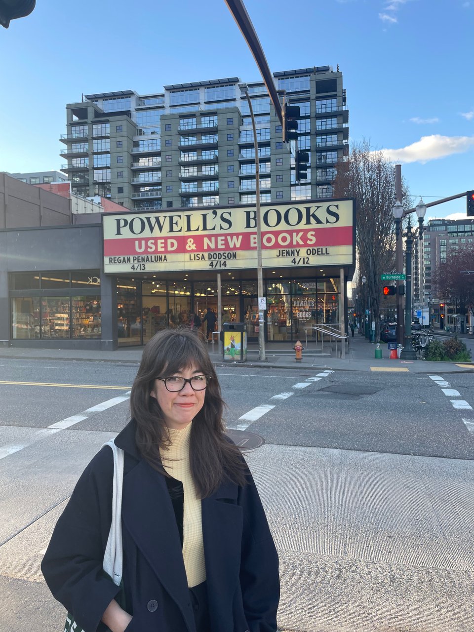 Jenny Odell stands across the street from Powell's Books in Portland. Her name is visible on the store's marquee, along with Regan Penaluma and Lisa Dodson.