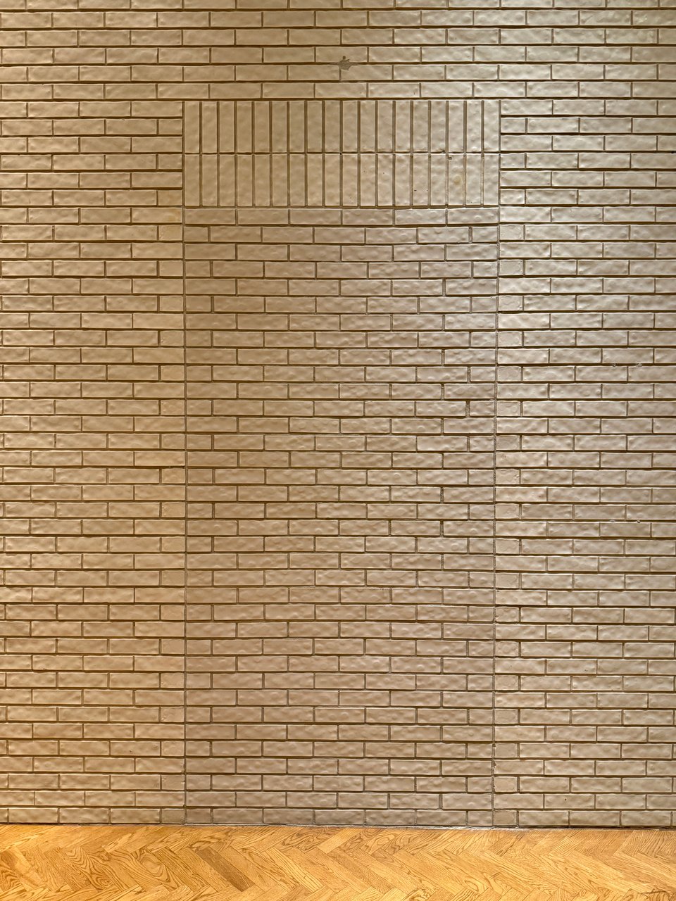 photo of a brick wall with parquet flooring. There's a section of the brick in a slightly darker shade, in the shape of a door, signifying where a door once was. Above it, there are two rows of vertically aligned bricks that could also be viewed as teeth if you were in a hallucinatory mindset