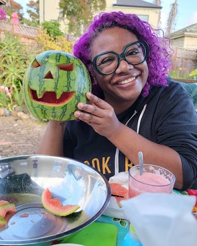 Patricia holding up a watermelon she carved with a Jack O'Lantern face