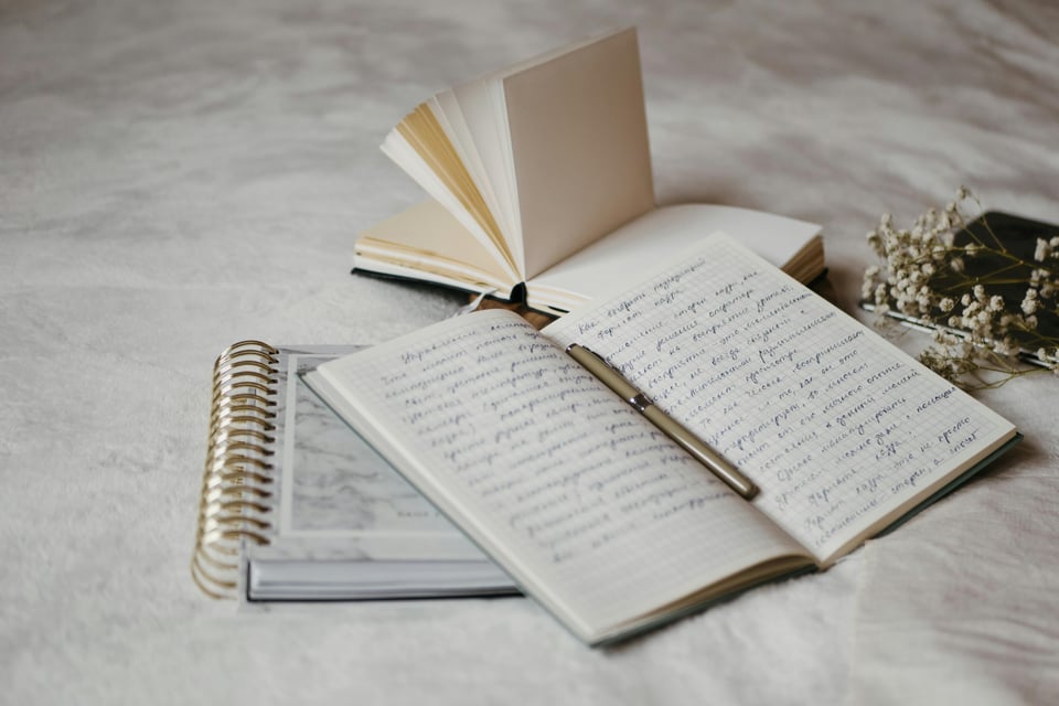Stock photo of an open notebook lying on top of other notebooks with words written in them that are unreadable.