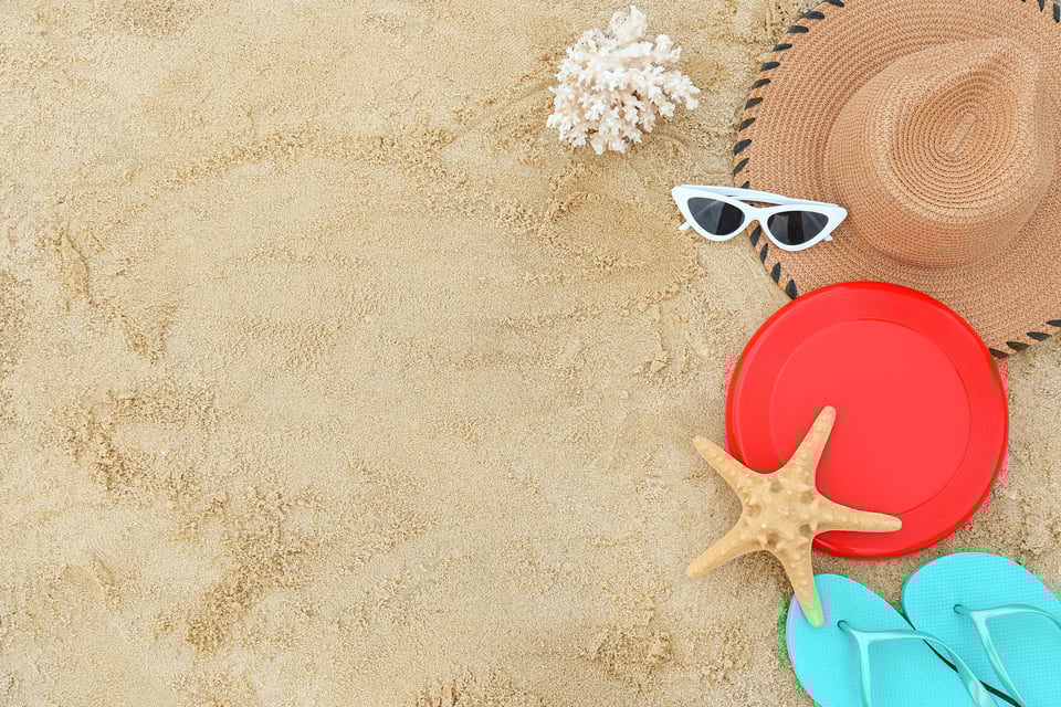 composition sur du sable. Il y a un chapeau, un corail, des lunettes de soleil, un frisbee, une étoile de mer, des tongs.