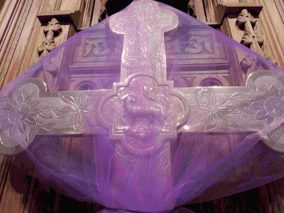 a golden cross with a lamb carrying a banner is shrouded with a transparent purple cloth