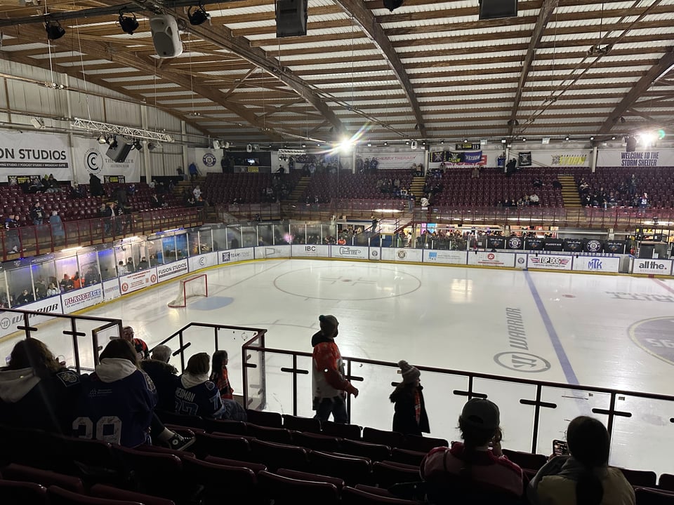 An ice rink surrounded by tiered seating. Above is an arched roof made from wooden beams.