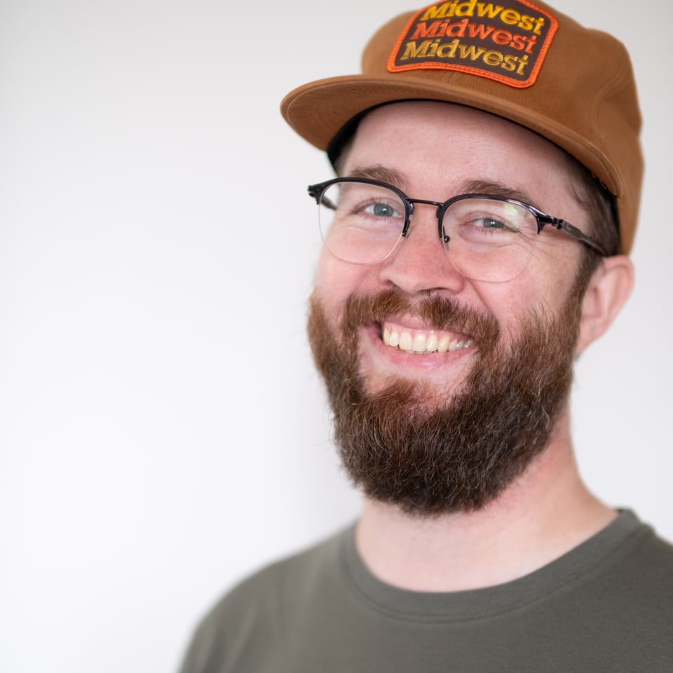 Micael Metts wearing a brown hat and standing in front of a white wall.