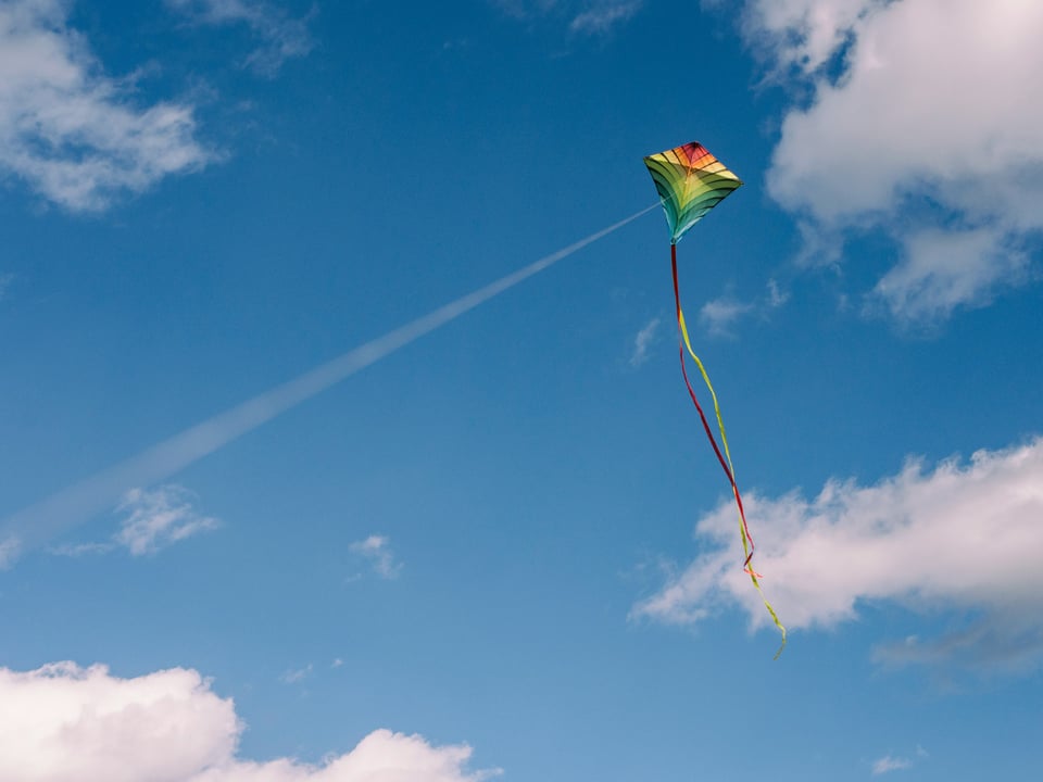 A rainbow coloured kite flies in a bright blue sky