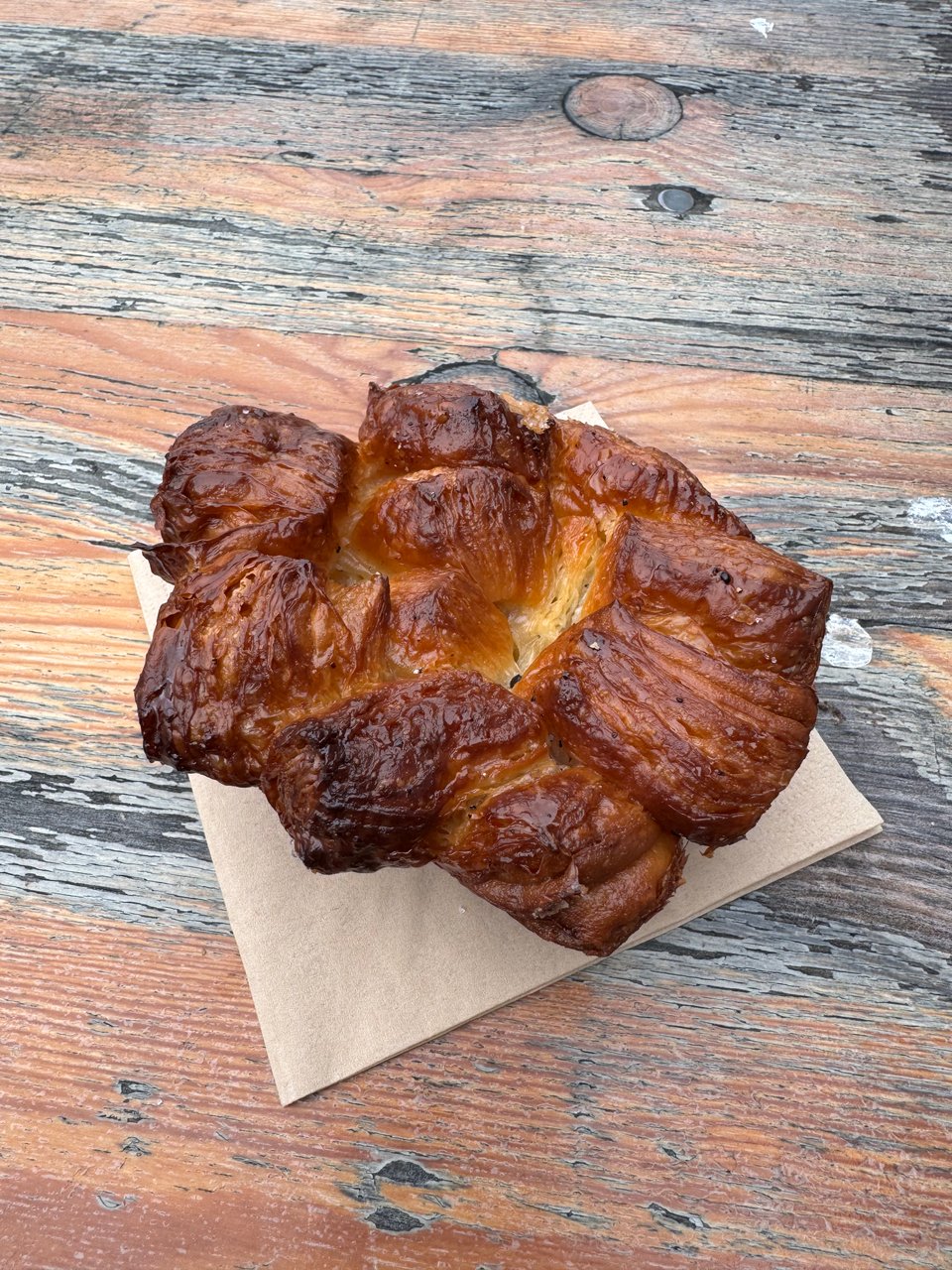 Looking top down at a perfectly baked cardamom bun, on a napkin, on a wooden surface.