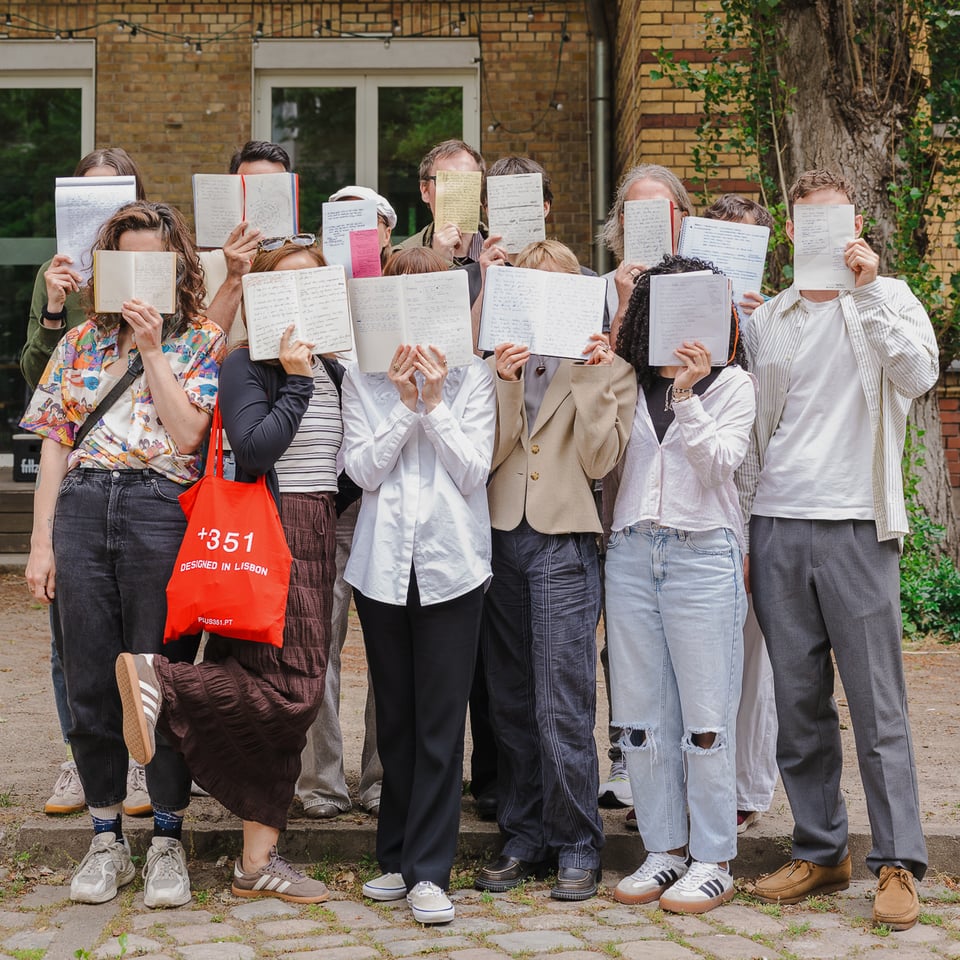 Group photo of the Writing = Design workshop participants: gathered outside, holding manuscripts in front of their faces