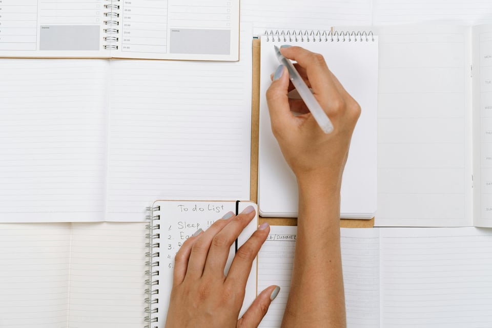 Image of a person (face not shown) writing in several open notebooks.