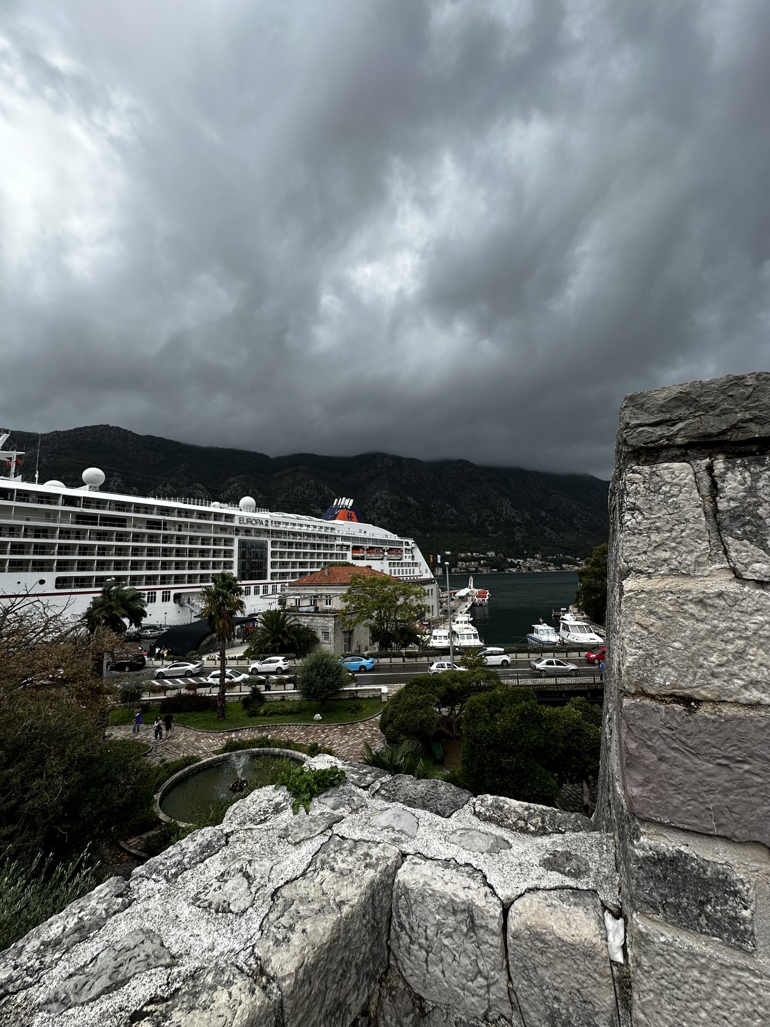 A cruise ship docked below Kotor's walls under storm clouds