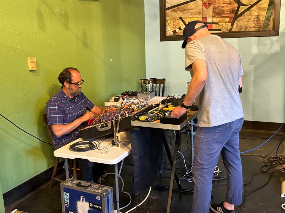 Free Static performing live with Chris Ruiz on the left, sitting at his synth and Courtney on the right, standing over a table of effects pedals