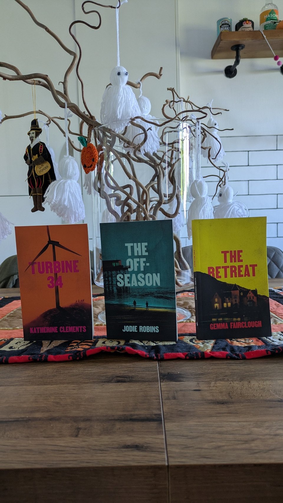 The covers of The Retreat by Gemma Fairclough, Turbine 34 by Katherine Clements and The Off-Season by Jodie Robins, in front of a brown and white halloween tree.
