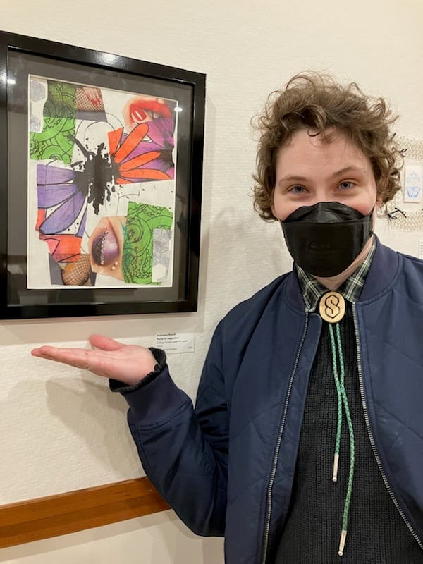 The artist, a white person in a black respirator mask, showing off their artwork, which is a vibrantly colored and mildly suggestive collage