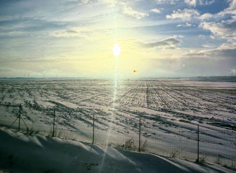 Countryside covered in snow with the weak sunlight shining over the field as seen through the train window. Countryside covered in snow with the weak sunlight shining over the field as seen through the train window.
