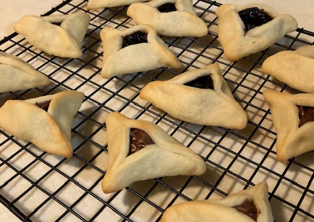 Hamentaschen (folded triangular cookies) filled with fig or chocolate on a wire baking rack